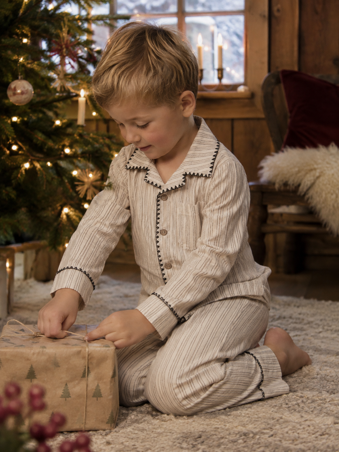 Gutt i Lil Atelier Sage stripete pysjamas pakker inn julegave ved juletreet