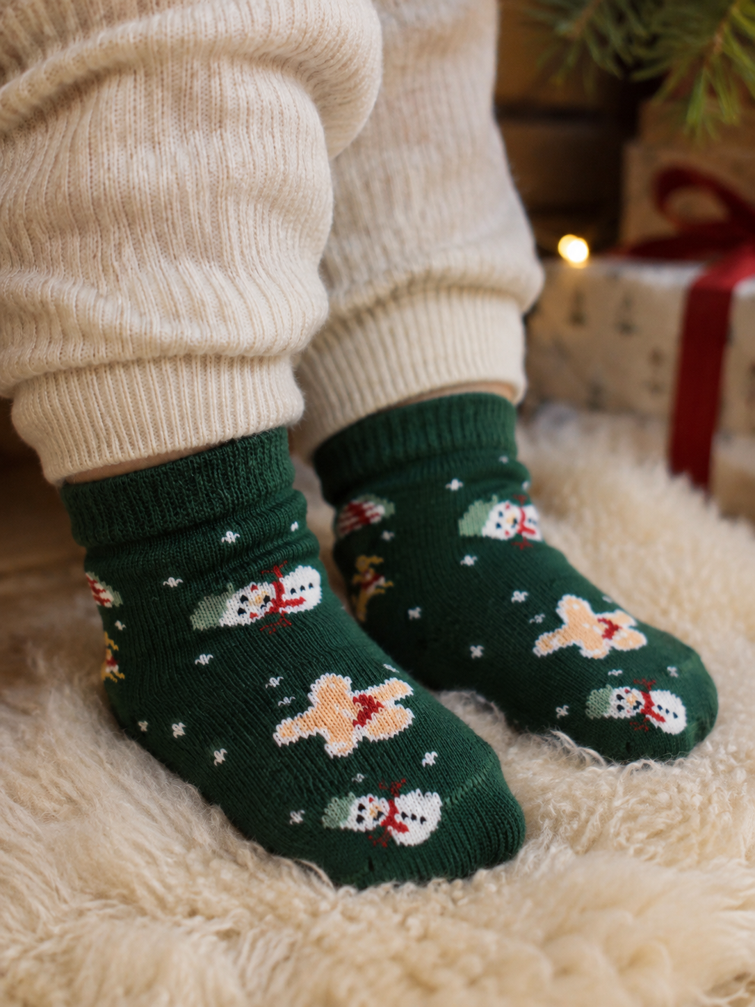 Babyføtter i Name it Vismas julesokker med snømenn på saueskinn ved juletreet