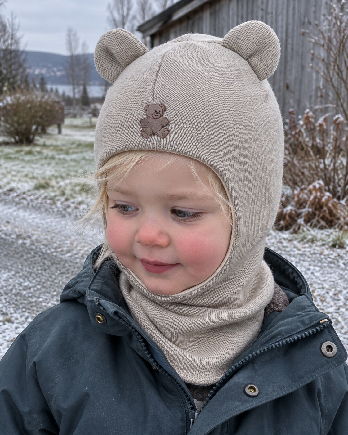 Liten jente i latte-farget Kivat-balaclava i ull med bamseører, ute en kald vinterdag