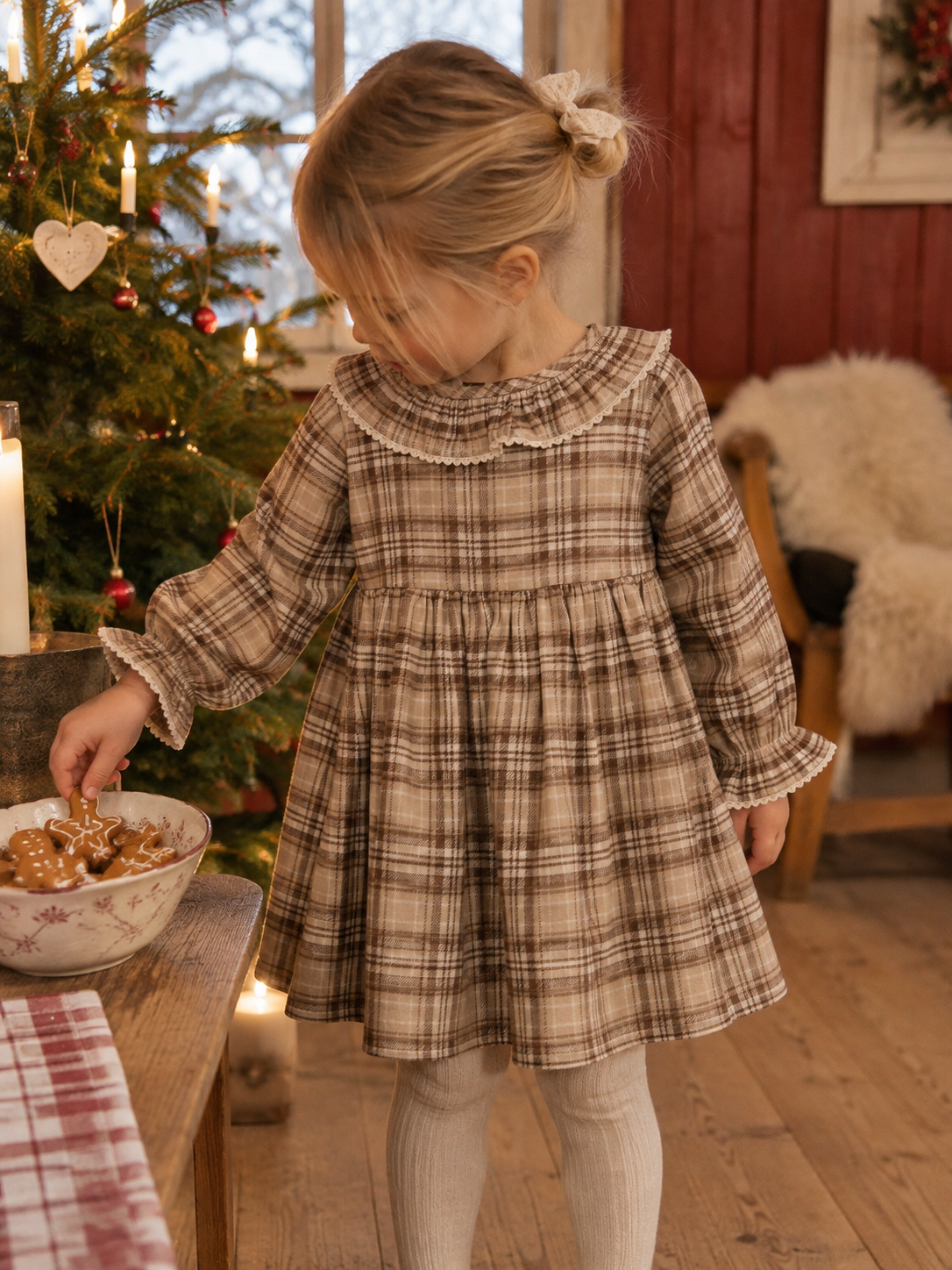 Jente i rutete Lil Atelier Renrik kjole med blondekrage i julepyntet gårdshus